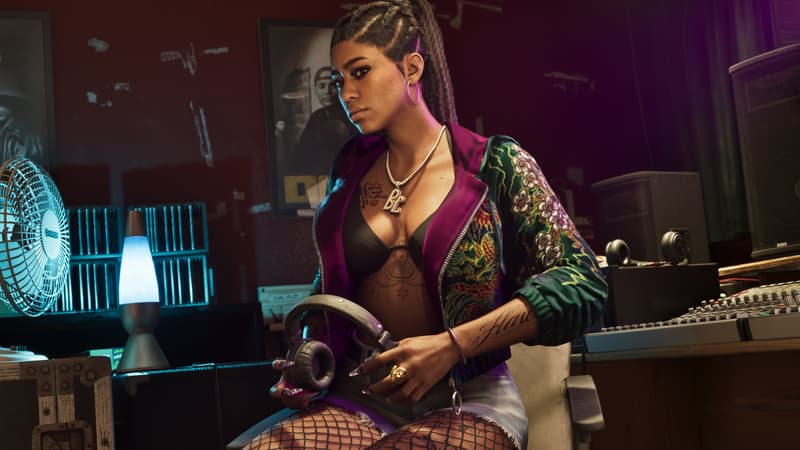 A woman with long braids and a diamond BL pendant sits at a studio mixing desk, holding headphones.