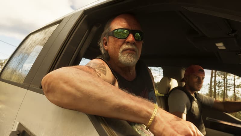 A grey-bearded man in wraparound sunglasses leans out of a truck window; a younger driver sits beside him.