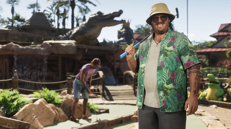 A grinning man in a bucket hat and leafy shirt shoulders a putter on a mini golf course with a giant gator statue.