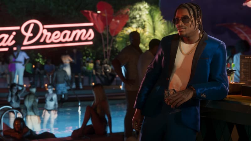 A man in a blue satin blazer holds a drink at the bar of a floodlit pool party, pink neon script behind.