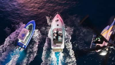 A speedboat cuts a wake with a police launch and a helicopter in pursuit above.
