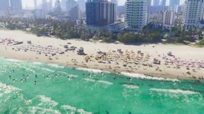 Aerial of beachfront hotel towers above umbrella-dotted sand and breaking surf