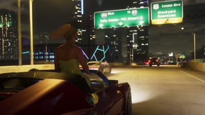 A woman rides the back of a convertible on a night freeway under airport exit signs