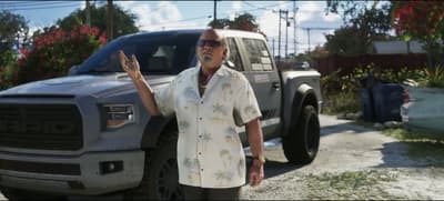 Brian Heder in a palm-print shirt gesturing beside his silver Vapid pickup truck