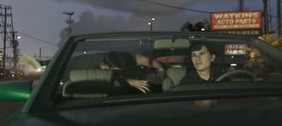 Jason and Lucia in a convertible, a third person climbing out over the back
