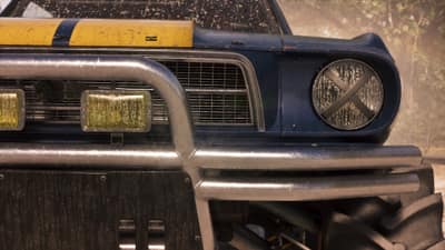 Mud-spattered tube bumper and a taped-over round headlight on a blue and yellow off-road car.