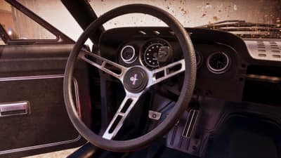 A worn muscle car's dished steering wheel and speedometer behind a mud-flecked windscreen.