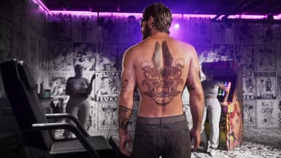 A shirtless man shows a large skull and wings back tattoo in a flash-papered studio.