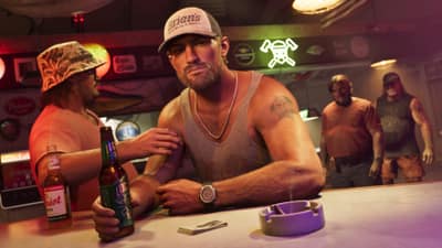 A man in a boatyard cap leans on a bar counter beside beer bottles and an ashtray.