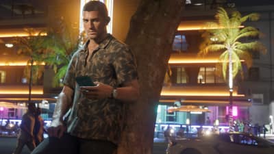 A man in a leaf-print shirt leans on a tree checking his phone on a neon-lit street.