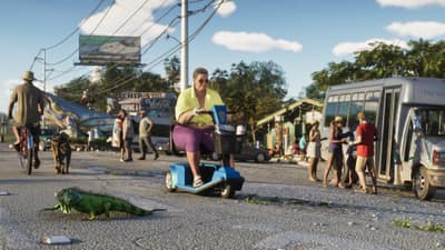 A man rides a mobility scooter down a sunlit street as an iguana crosses in front.