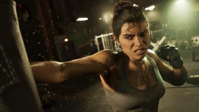 A woman in a sports bra and fingerless gloves throws a punch at a heavy bag.