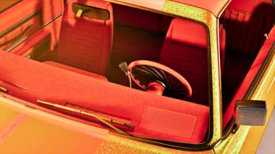 Looking down into a lowrider's red velour bench seats and thin chain-link steering wheel.