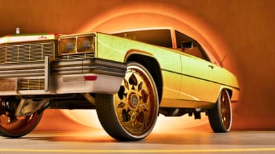 A gold-flake lowrider sedan on gold wire wheels lit against a glowing orange studio wall.