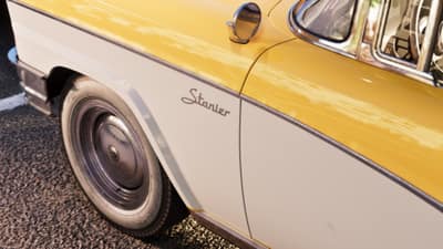 The front wing of a yellow and white fifties sedan showing its script Stanier badge.