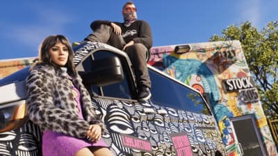 A woman in a fur coat and a masked man sit on a graffiti-wrapped van outside a store.