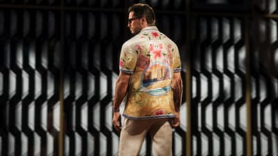 Back view of a man in a bowling shirt printed with flamingos and a beachfront scene.