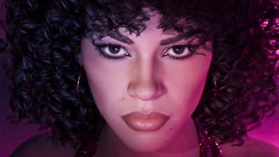 Close portrait of a woman with large curled eighties hair and hoop earrings under pink light.