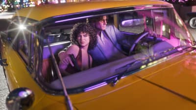 A couple ride in a yellow fifties sedan at night, the passenger resting a pistol on the door.