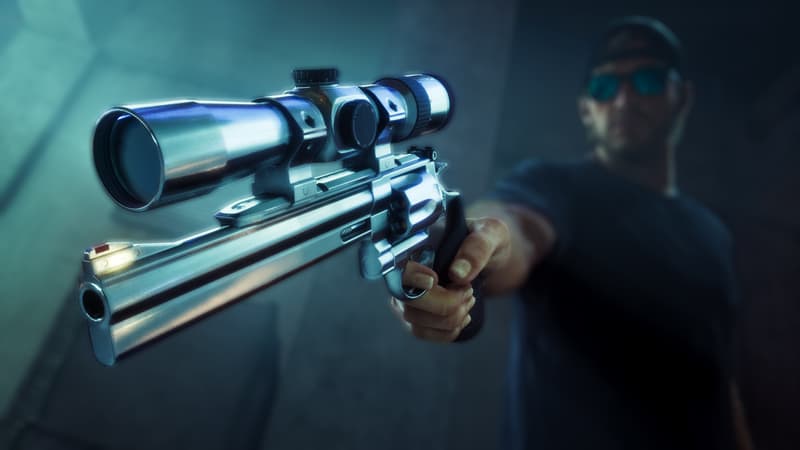 A man in a cap and sunglasses levels a long-barrelled stainless revolver fitted with a telescopic sight.