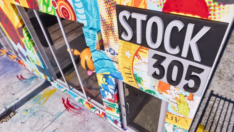 A raised sign reading Stock 305 juts from a storefront wall covered in layered spray-painted murals.