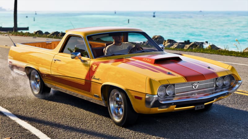 A yellow and red coupe utility badged Ganado drives a sunlit coastal road lined with palms.